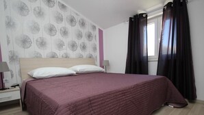 A bedroom with a large bed, a nightstand, a lamp, and a window with curtains. - Apartment Gorica by Interhome (Krk/Baška)