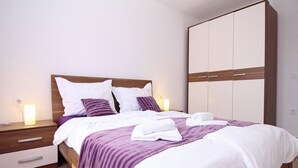 A neatly made bed with white and purple bedding, a wooden headboard, and a large wardrobe with two doors. - Appartement in Baška mit Terrasse by Interhome (Krk/Baška)