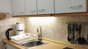 Keittiössä on valkoiset kaapit, ruostumattomasta teräksestä valmistettu pesuallas ja kahvinkeitin.