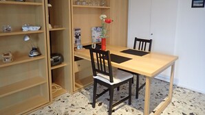 Ruokailutila, jossa on puinen pöytä ja tuolit, ja jonka ympärillä on avohyllyjä, joissa on erilaisia esineitä.