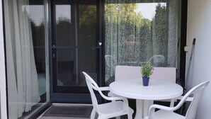 Parvekkeella on lasiovi, valkoiset muovituolit, pyöreä valkoinen pöytä ja ruukussa oleva kasvi.