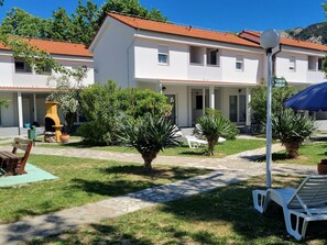 A two-story building with a red-tiled roof, a covered outdoor seating area, and a fire escape sign. - Ville Corinthia 1 by Interhome (Krk/Baška)