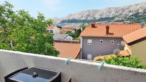 En balkong med ett bord och stolar, med utsikt över ett bostadsområde med hus och berg i bakgrunden.