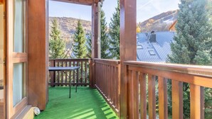 Un balcón de madera con una mesa y sillas, piso de césped artificial verde y vista a una montaña y árboles.