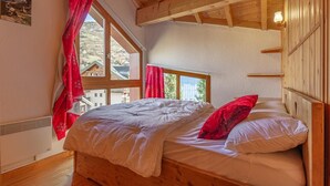 Un dormitorio con cama de madera, cortinas rojas y ventana con vista a la montaña.