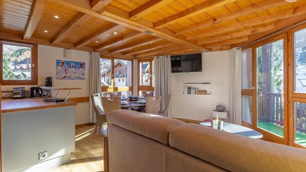 Una habitación acogedora con techo de madera, un sofá, una mesa de comedor y un televisor.
