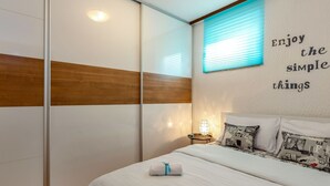 Een slaapkamer met een bed, kussens, een nachtkastje en een muur met een inspirerende quote.