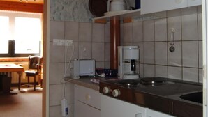 A compact kitchen with white cabinets, a stove, a coffee maker, and a sink. - Wohnung in Goosefeld mit Grill by Interhome (Eckernförde)