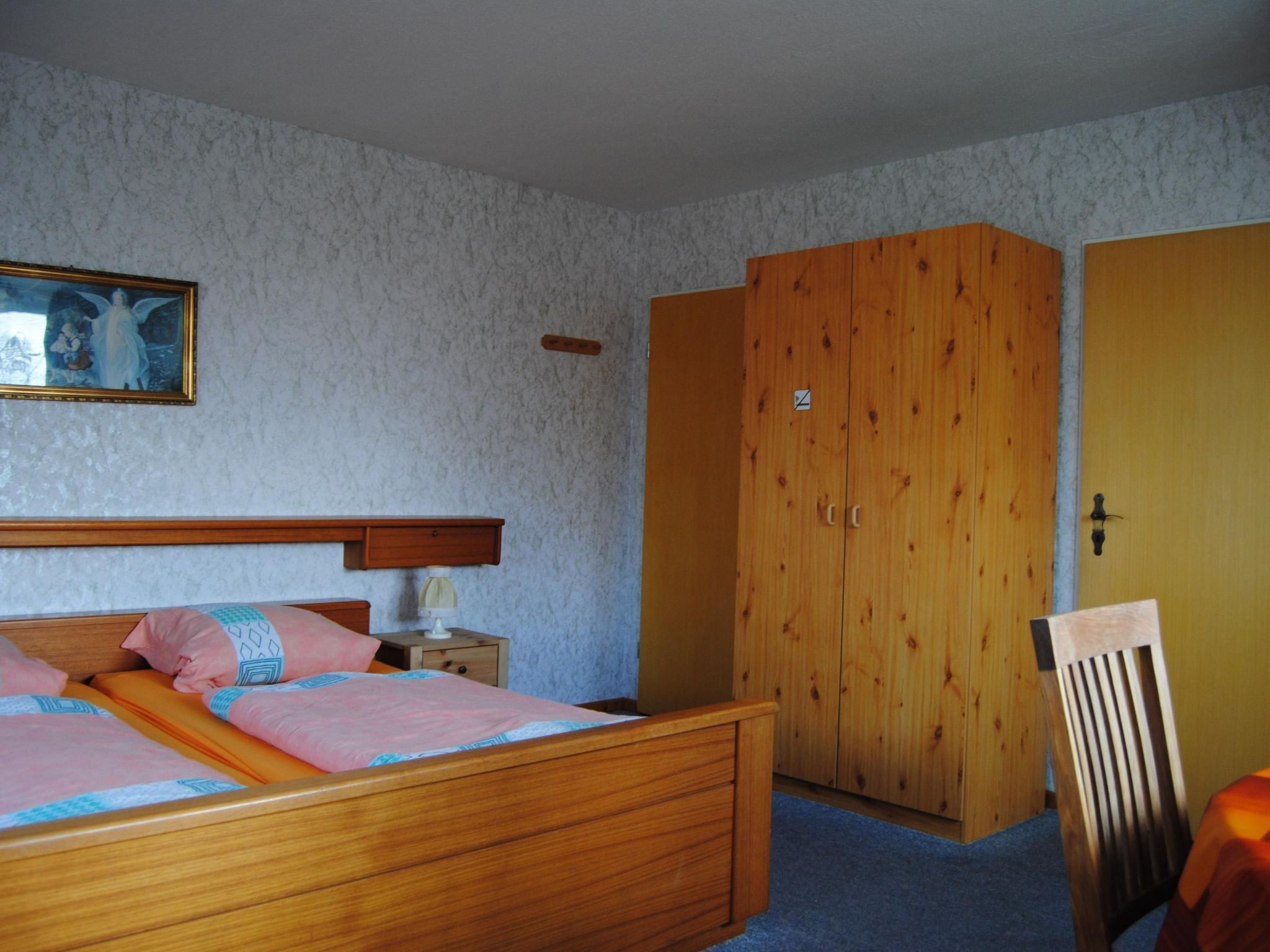A bedroom with a wooden bed, a nightstand, a wardrobe, and a chair.