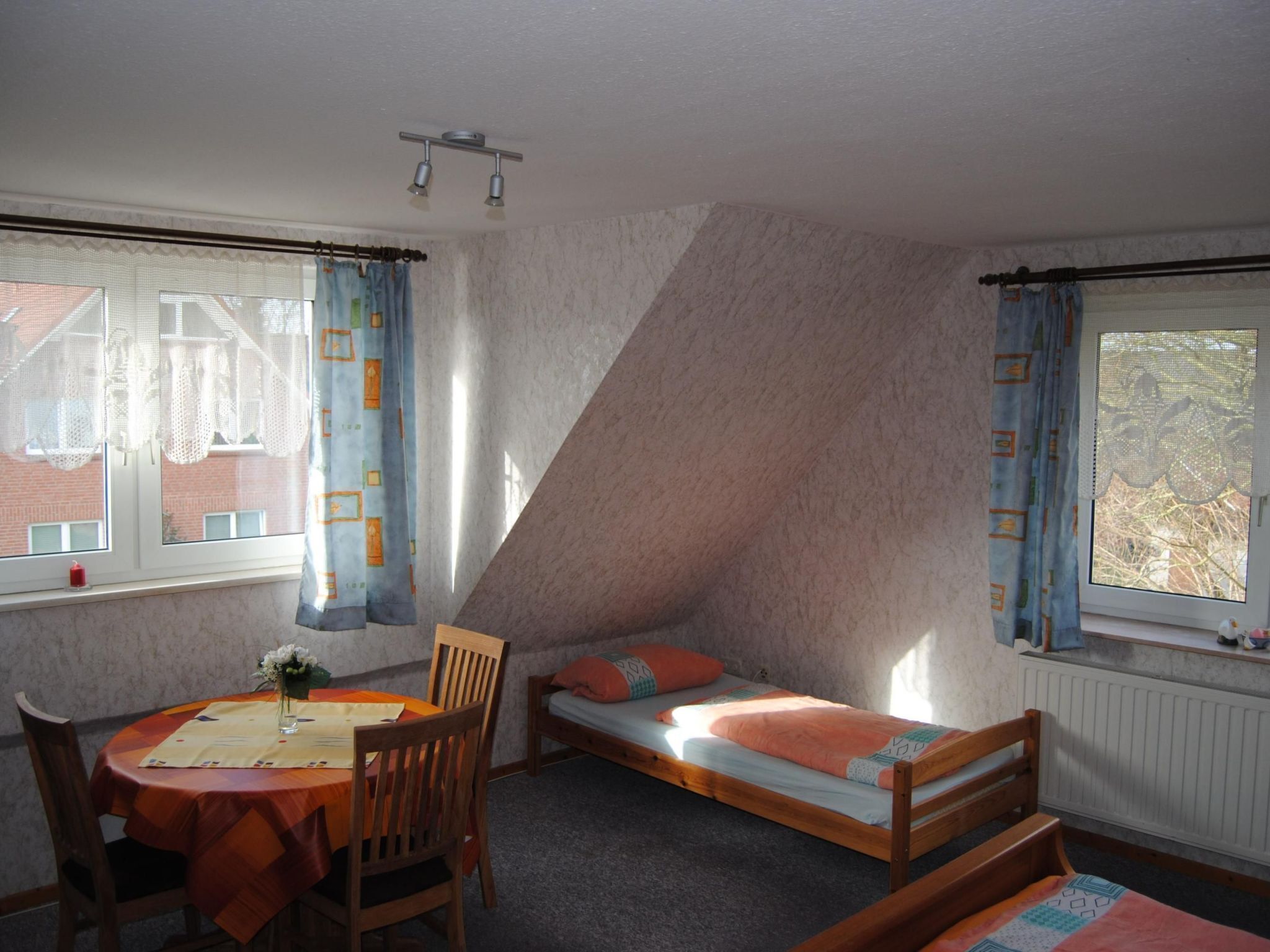 Um quarto com uma cama de solteiro, uma mesa de jantar com cadeiras e uma janela com cortinas.