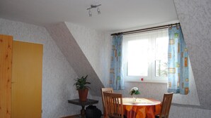 Ein Schlafzimmer mit einem Bett, einem kleinen Tisch mit Pflanze und einem Fenster mit Vorhängen.