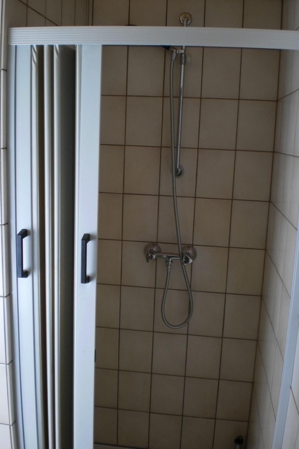 Suihkukaappi, jossa on valkoinen ovi ja laatoitettu seinä.