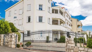 Un edificio de varios pisos con entrada protegida por una reja, paredes exteriores blancas y varios balcones.