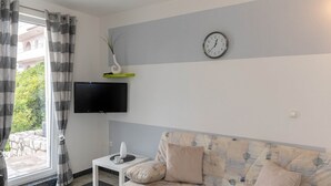 Uma sala de estar com um sofá, uma mesa de centro, uma televisão de tela plana e um relógio de parede.