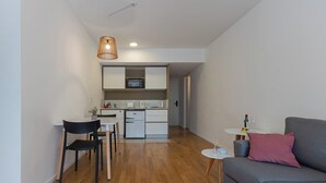 A compact living space with a dining area, kitchenette, and a gray sofa with a pink pillow. - Modern Studio Apartment Full Amenities in Palermo (Buenos Aires)