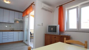 A compact kitchen with white cabinets, a wooden table, and a television on a wooden cabinet. - Wohnung in Baška mit Eigenem Balkon by Interhome (Krk/Baška)