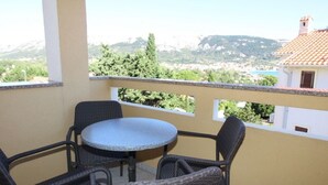 A balcony with wicker furniture and a round table, overlooking a scenic landscape with mountains and buildings. - Wohnung in Baška mit Eigenem Balkon by Interhome (Krk/Baška)