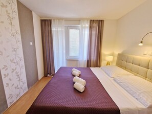 Una camera d'albergo con un letto, una finestra con tende, una lampada da comodino e una parete con motivo floreale.