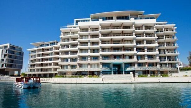 Un hotel de varios pisos con balcones, vista al agua y un barco amarrado cerca.