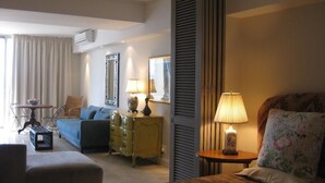 Una habitación de hotel con cama, sofá, una mesita, cómoda y ventana con cortinas.