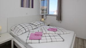 A bedroom with a bed, pillows, a bedside table, a lamp, a window with curtains, and a painting on the wall. - Lavanda4 by Interhome (Krk/Baška)