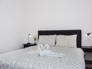 A neatly made bed with a patterned bedspread, two bedside tables with lamps, and a vase with flowers on one of the tables. - Charmantes Appartement in Baška mit Eigenem Balkon by Interhome (Krk/Baška)