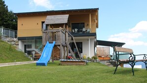 Una casa moderna con una terrazza in legno, uno scivolo blu e una panchina.