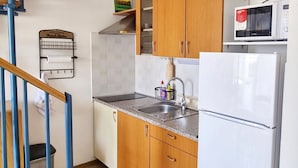 A kitchen with wooden cabinets, a stainless steel sink, a microwave, and a refrigerator. - in Baska in der Nähe von Strand by Interhome (Krk/Baška)