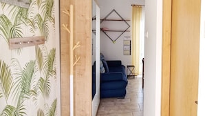 A hallway with a wooden door, a blue sofa, a wall calendar, and a plant shelf. - in Baska in der Nähe von Strand by Interhome (Krk/Baška)