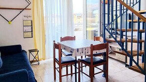 A dining area with a table and chairs, a sofa, a staircase, and a view through a glass door. - in Baska in der Nähe von Strand by Interhome (Krk/Baška)