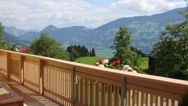 Un balcon offrant une vue sur des collines verdoyantes et des montagnes, sous un ciel dégagé.