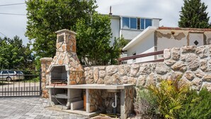 A stone-built outdoor kitchen area with a chimney, surrounded by a paved walkway and greenery. - Appartement in Baška mit Eigenem Balkon by Interhome (Krk/Baška)
