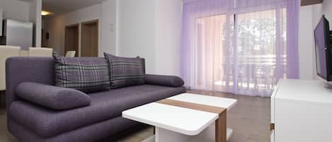 A modern living room with a purple sofa, a white coffee table, and a TV on a white cabinet.