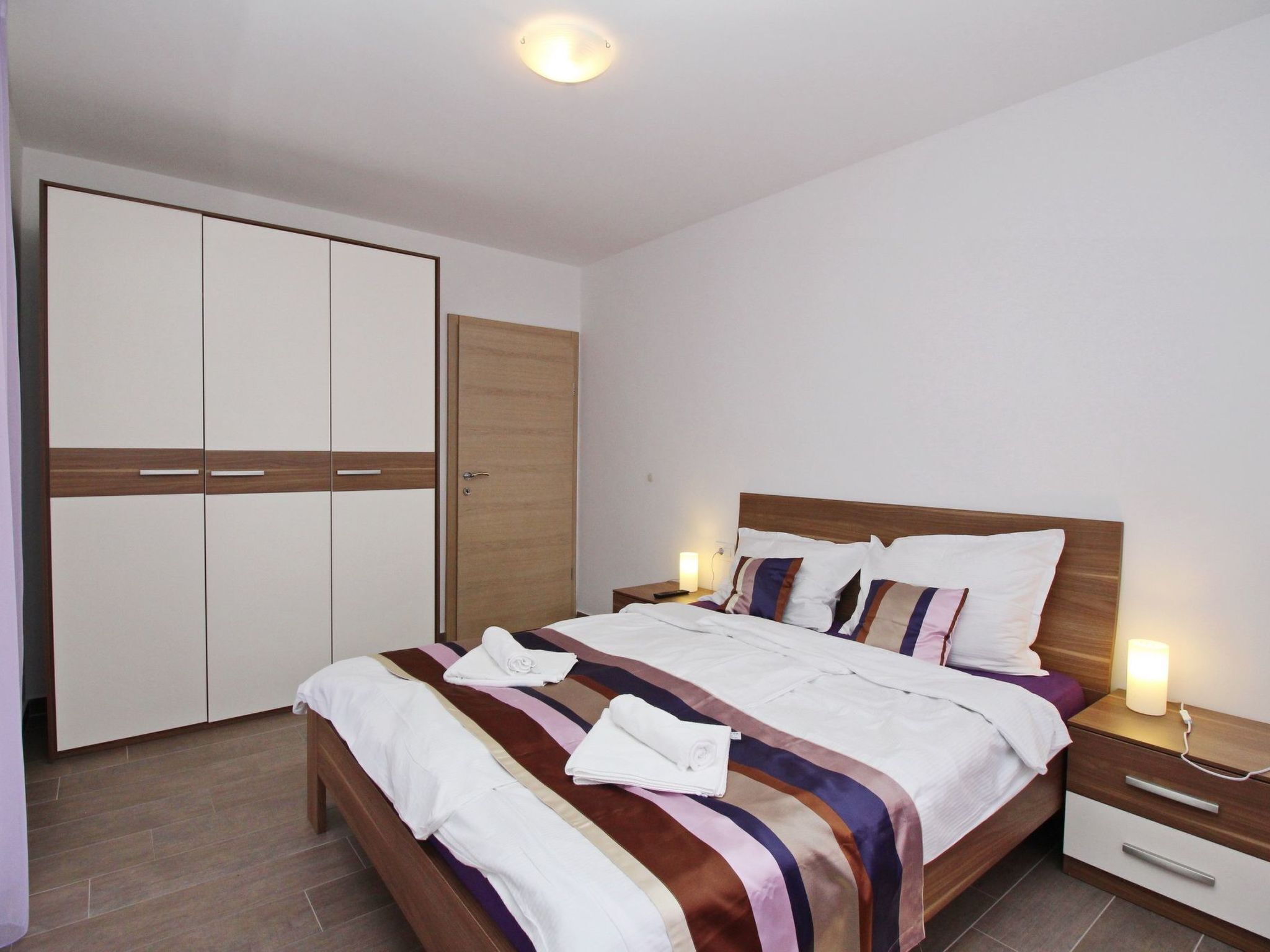A neatly arranged bedroom with a bed, bedside tables, a wardrobe, and a nightstand.