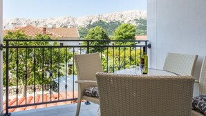 Een balkon met rieten stoelen en een tafel, met uitzicht op een bergachtig landschap met terracotta daken.