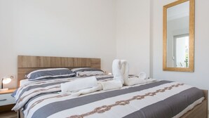 Een net opgemaakt bed met een gestreept sprei, een houten hoofdbord en een grote spiegel aan de muur.