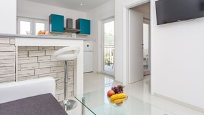 Een moderne keuken met blauwgroene kastjes, een betegelde achterwand en een glazen eettafel met fruit.