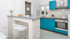 Een moderne keuken met een stenen keukeneiland, blauwe kastjes en roestvrijstalen apparatuur.