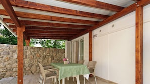 En overdækket terrasse med et bord og stole, en stenvæg og en dør, der fører til en garage.