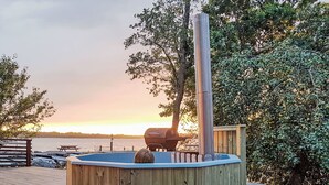 A wooden deck with a hot tub, a barbecue grill, and a view of the water. - Holzhaus mit überdachter Terrasse by Interhome (Bräkne-Hoby)