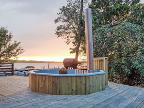 A wooden deck with a hot tub, a barbecue grill, and a view of the water. - Holzhaus mit überdachter Terrasse by Interhome (Bräkne-Hoby)