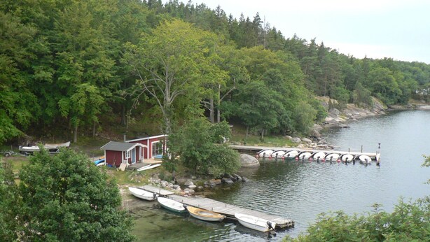 A lakeside cabin with docked boats, surrounded by dense forest. - Holzhaus mit überdachter Terrasse by Interhome (Bräkne-Hoby)