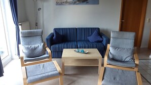 Een woonkamer met een blauw gestreepte bank, twee grijze fauteuils en een houten salontafel.
