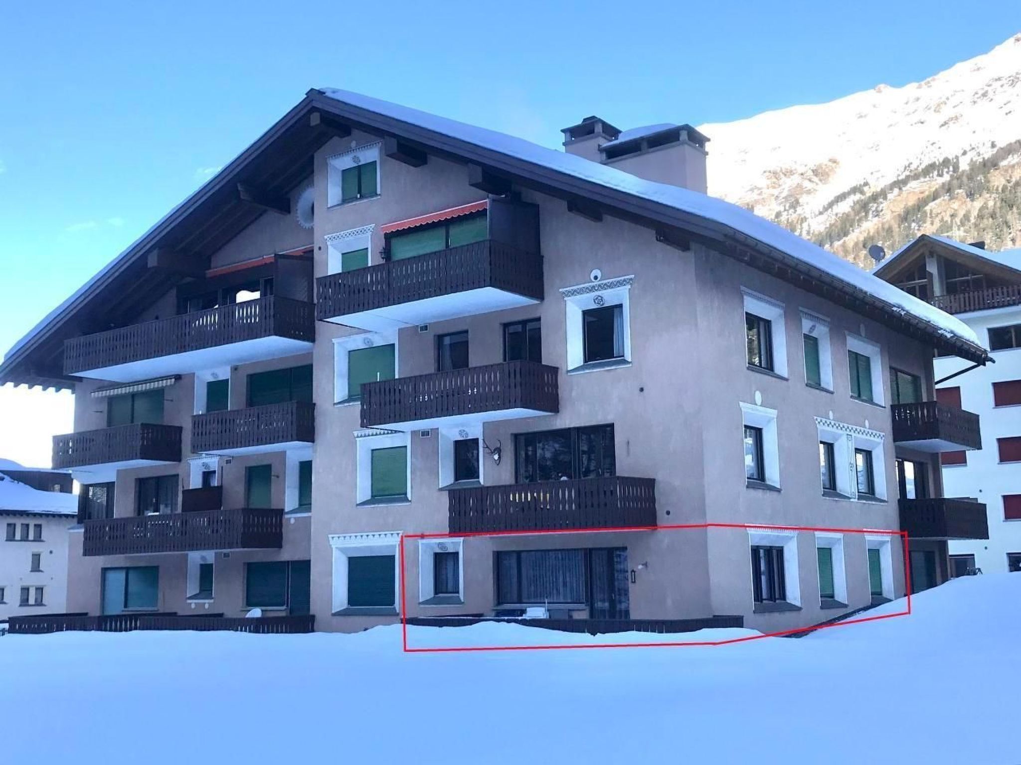Un immeuble à plusieurs étages doté de balcons, d’un toit enneigé et surplombant un paysage montagneux.