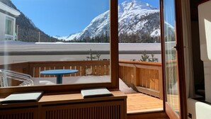 Una habitación con banca y mesa de madera, amplias ventanas con vistas a montañas nevadas.