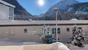 Un edificio cubierto de nieve con montañas al fondo, cielo despejado y una farola.