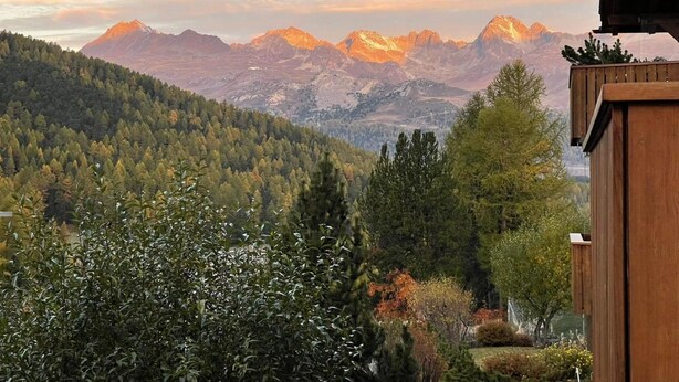 Un paisaje montañoso con vistas a picos nevados y un valle boscoso.