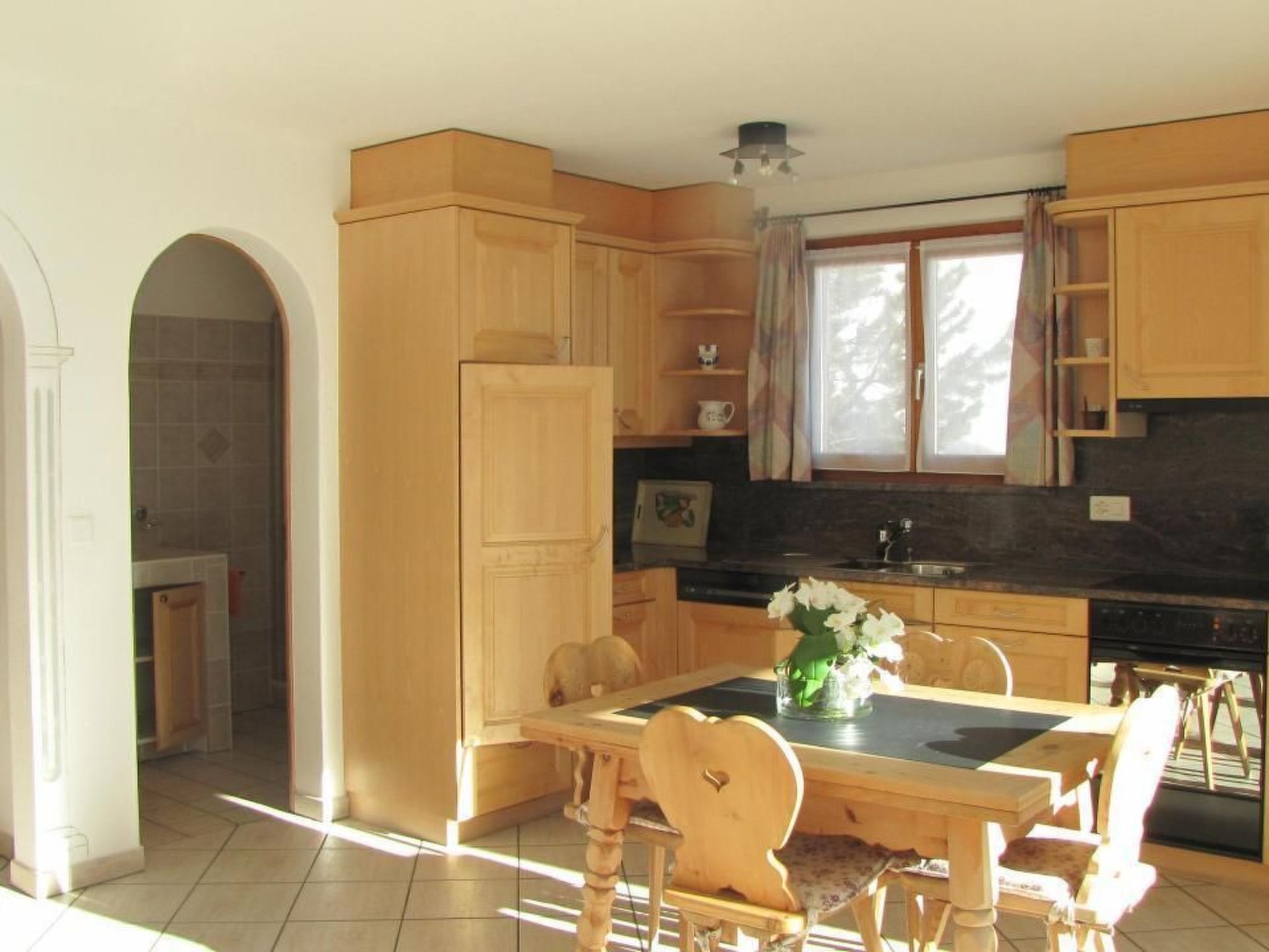 A kitchen with wooden cabinets, a dining table with chairs, and a window with curtains.