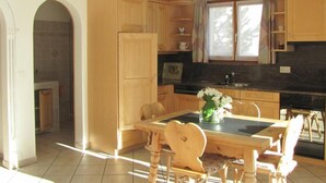 A kitchen with wooden cabinets, a dining table with chairs, and a window with curtains. - Chesa Ovelin by Interhome (Pontresina)
