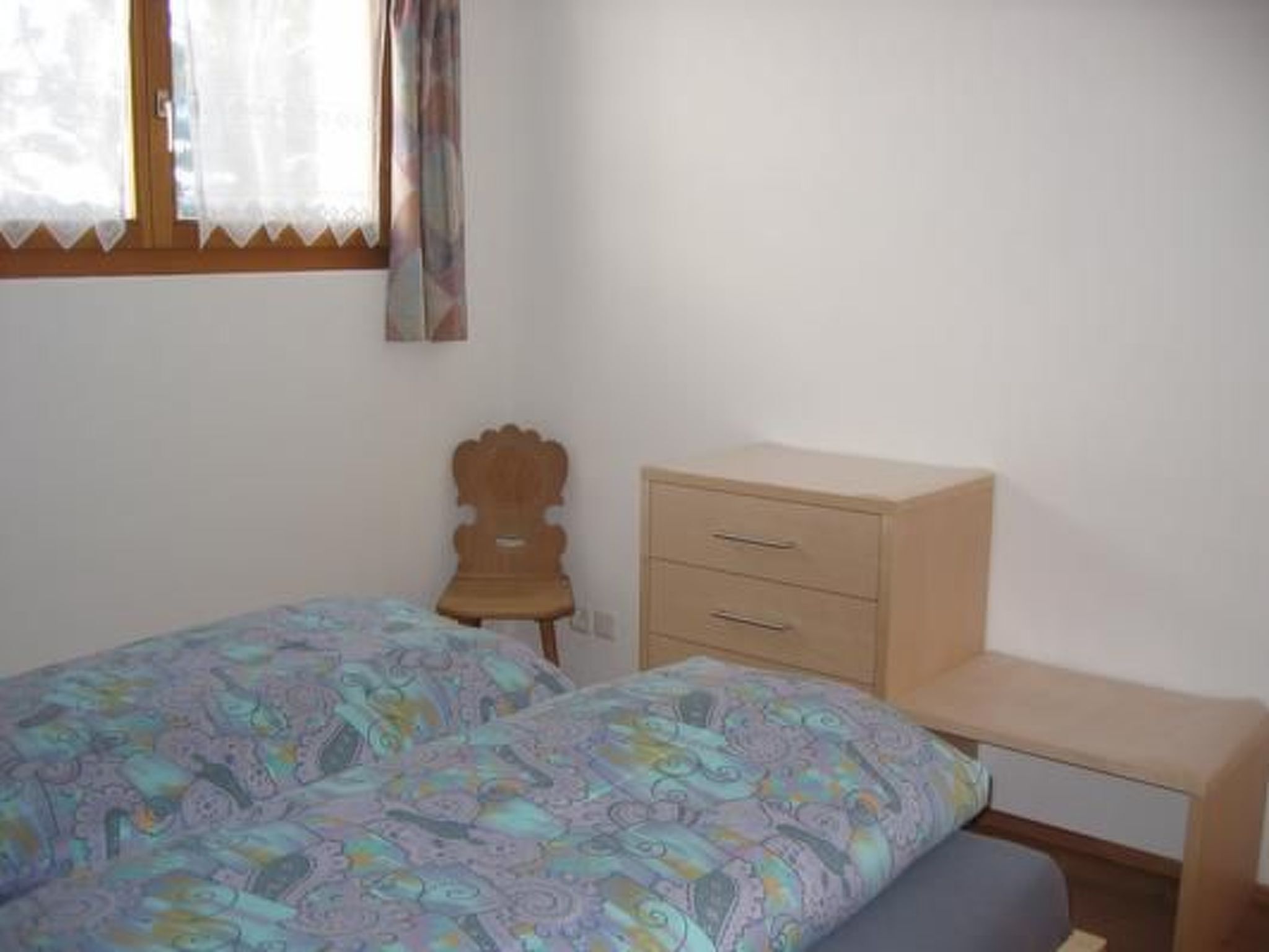 Un dormitorio con dos camas individuales, una mesita de noche de madera, un aparador y una ventana con cortinas.